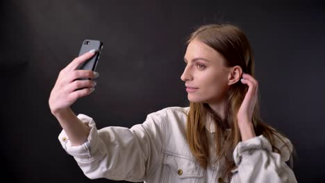 young cool girl is making selfie on smartphone, touching hair, communication concept, grey background