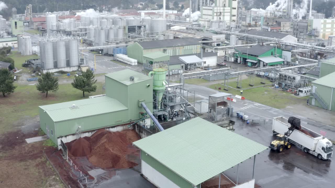 Aerial circling shot of industrial factory complex, truck unloading wood chips, silos, Veille-Saint-Girons, France