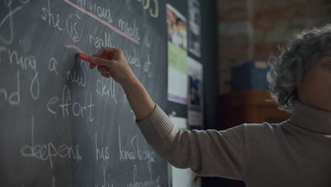 english teacher pointing at blackboard and talking to students in classroom