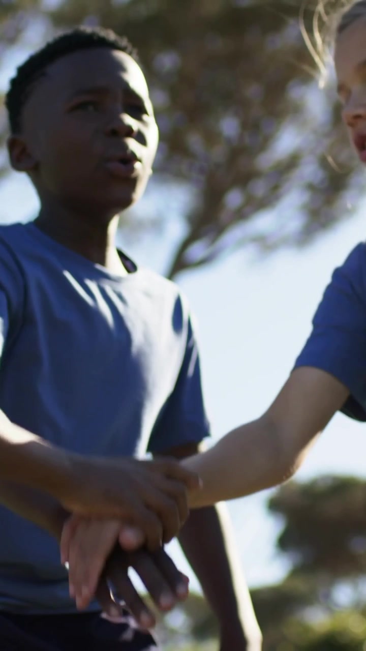 Vertical video: Stacking hands boy in blue tee chanting park, raising small red ball to start game