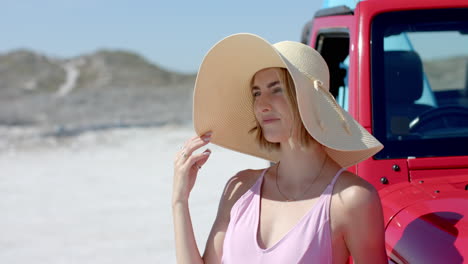 young caucasian woman poses by a red car on a road trip with copy space