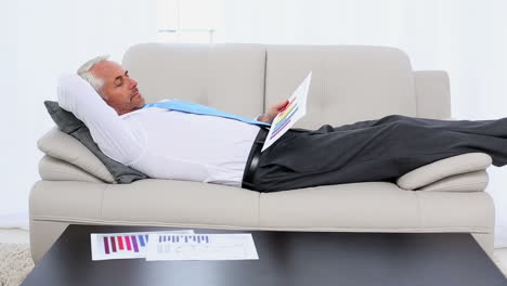 businessman falling asleep holding paperwork on the couch