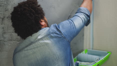 Afro-American guy in denim shirt and gloves paints corner