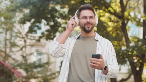 happy young man putting on headphones listening favorite energetic music in smartphone on street