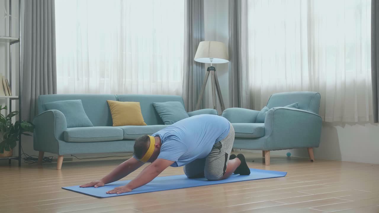 hombre gordo asiático haciendo yoga mirando hacia arriba hacia adelante doblarse en la alfombra en casa