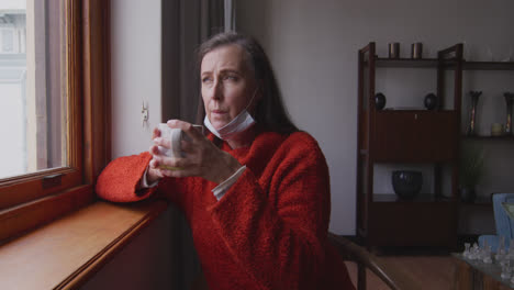 woman drinking coffee while looking out of the window at home