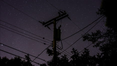 a time-lapse of the stars rotating in the sky behind a silhouetted suburban telephone pole and power lines and trees in the night sky