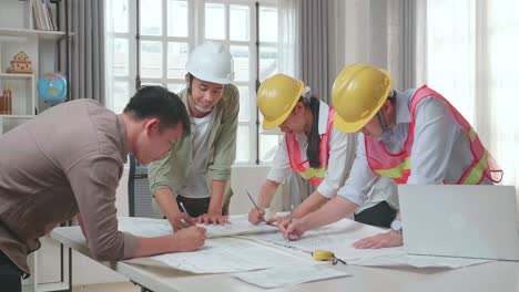 three asian engineers with helmets helping a man drawing building construction at the office