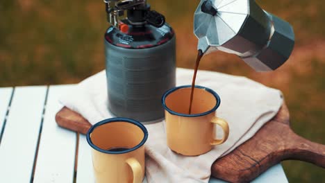 Während-Des-Campings-Gießt-Er-Kaffee-Aus-Einem-Silbernen,-Kompakten-Metallkessel-In-Einen-Gelben,-Robusten-Becher