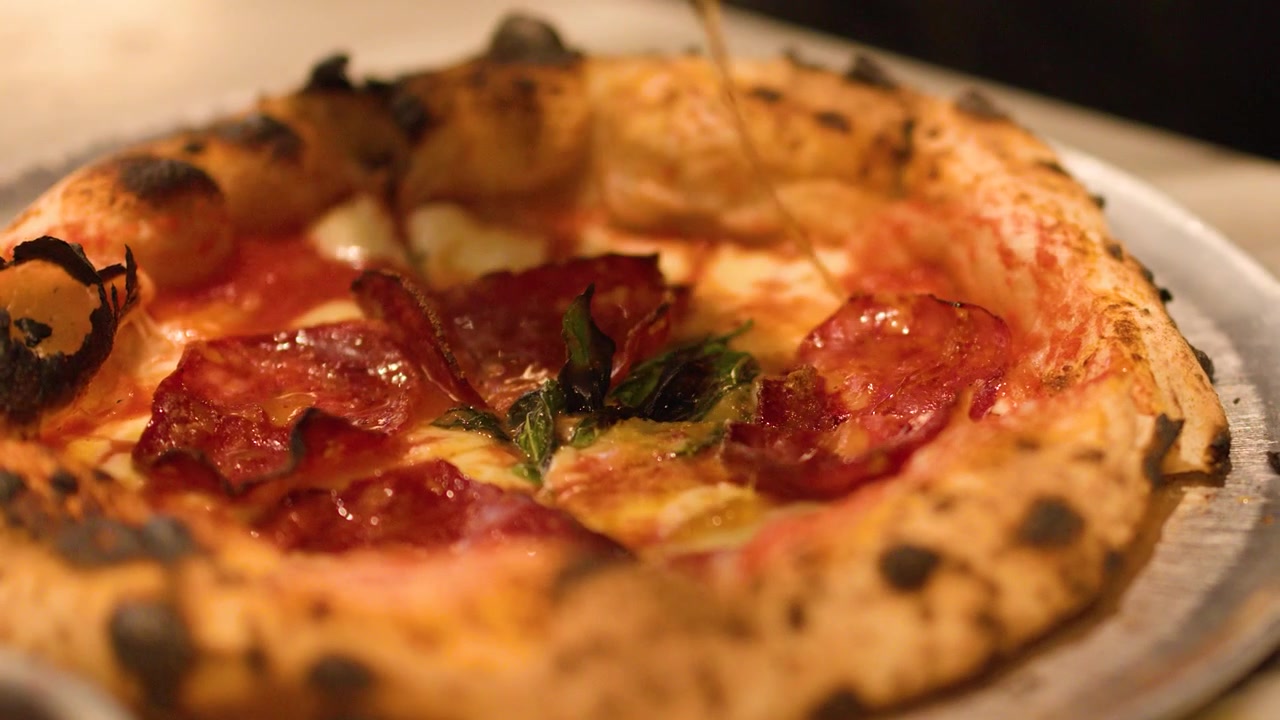 Chef che irrora olio su pizza al salame piccante appena sfornata
