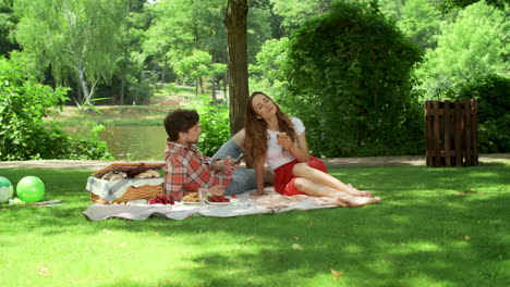 pareja haciendo un picnic en el parque. mujer sonriente y hombre usando teléfonos inteligentes al aire libre