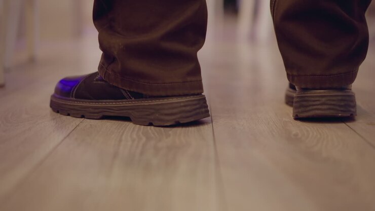 Close-up shot of man s feet walking on wooden floor, wearing brown shoes, with motion blurring and smooth floor texture visible, indicating movement in indoor setting with focus on ground