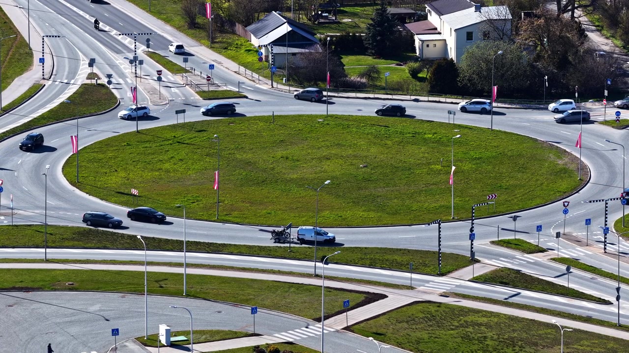 Aerial view of cars driving on a city traffic roundabout with a green grass island in slow motion