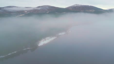 Descending-through-the-thick-mist-to-reveal-campers-on-snow-covered-lakeside