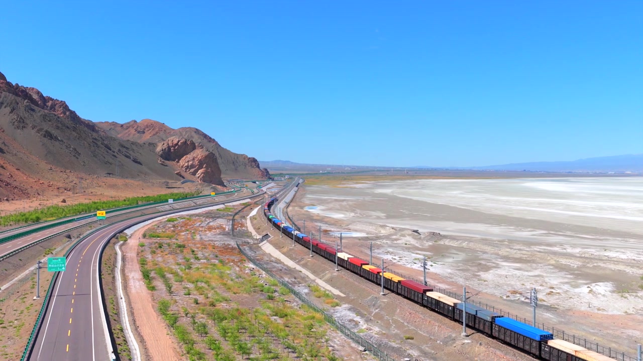 Vista aerea di un treno merci al porto di Alashankou lungo la Via della Seta nello Xinjiang, ferrovia merci Cina-Europa che attraversa una zona di confine montuosa arida. Trasporto commerciale internazionale della Belt and Road.