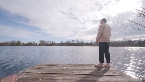 young man standing alone on wooden footbridge and staring at lake. thinking about life. peaceful atmosphere in nature. enjoying fresh air. back view.