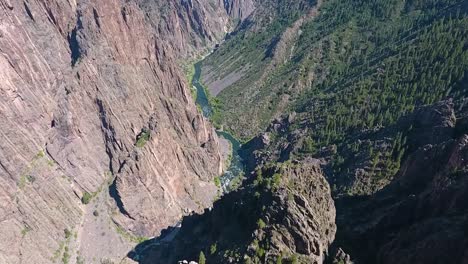 A-fly-over-drone-shot-panning-down-into-Black-Canyon,-an-extreme,-steep-walled-gorge,-containing-massive-rock-spires,-carved-out-by-the-Gunnison-River,-in-Gunnison-National-Park,-in-Western-Colorado