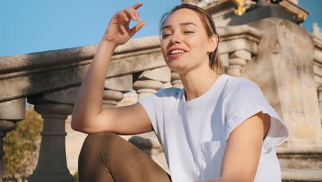 Mujer-Felizmente-Hablando-A-La-Cámara-Descansando-En-Las-Escaleras-Bajo-El-Sol-Al-Aire-Libre.