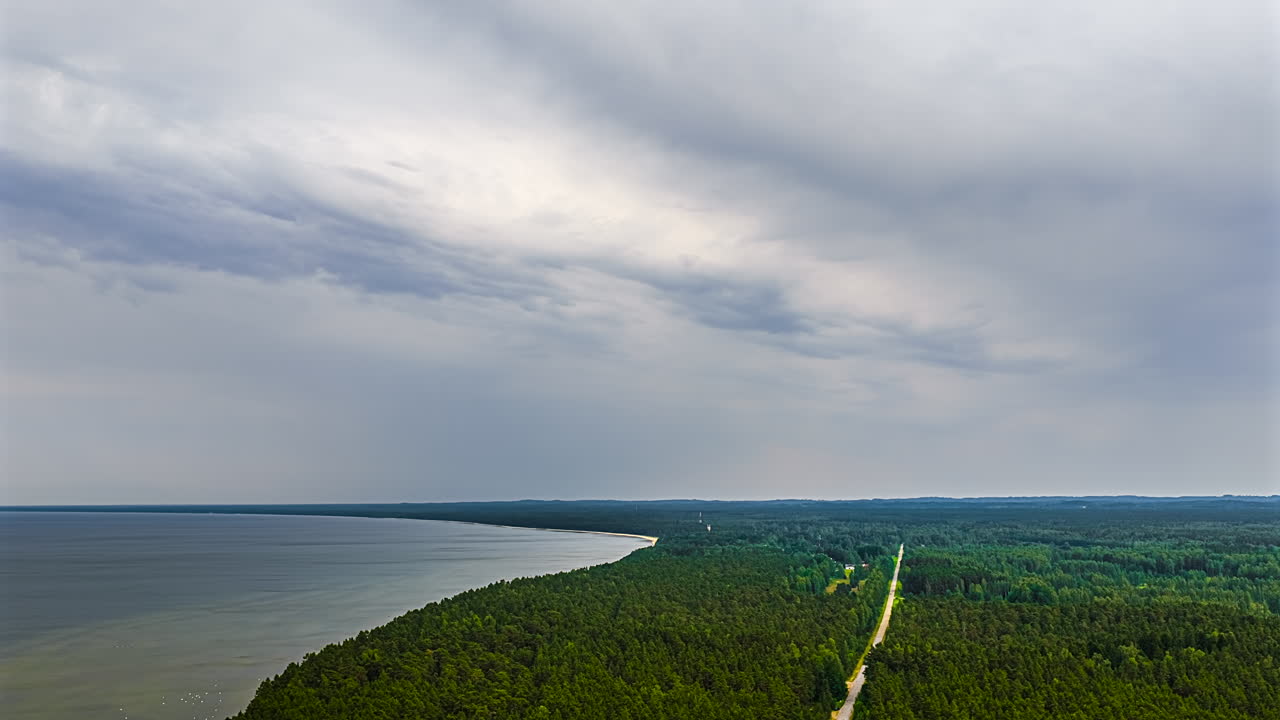 Overcast sky over forested coastline and open water, gray tones and calm atmosphere, timelapse