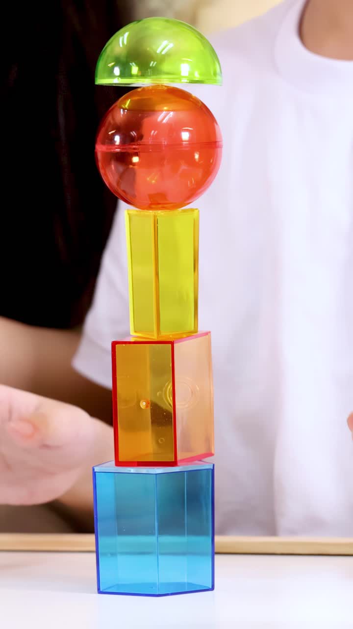 Primer plano de un adulto montando una torre alta con bloques magnéticos translúcidos bajo una brillante iluminación de estudio