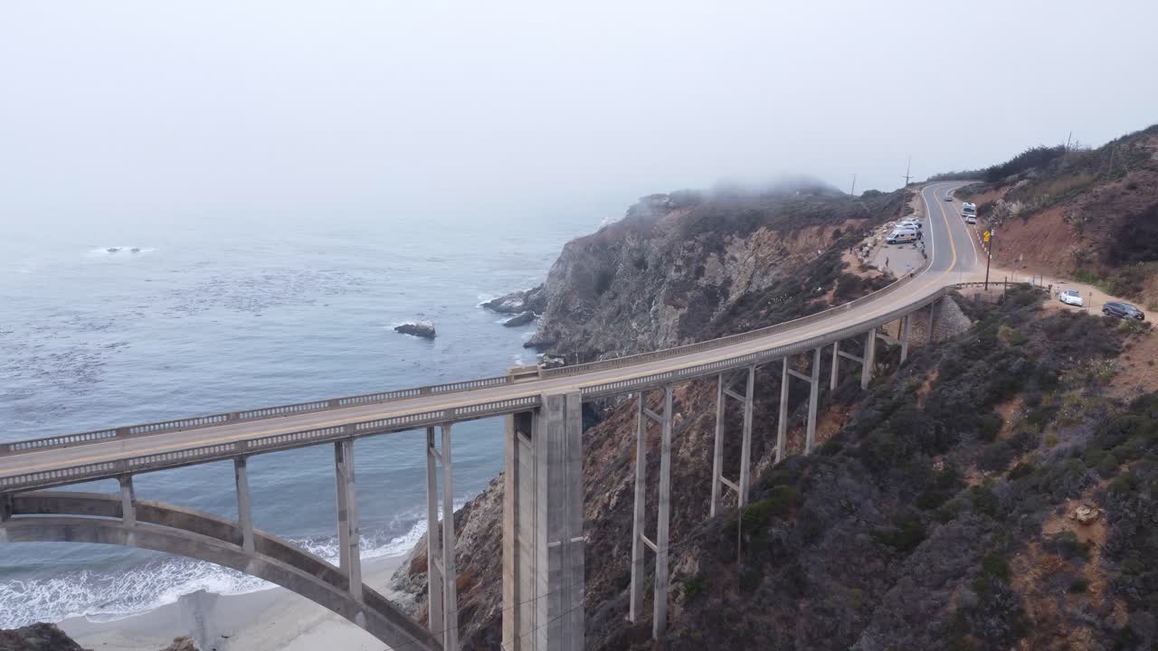 A drone shot passing over a bridge next to the coast.