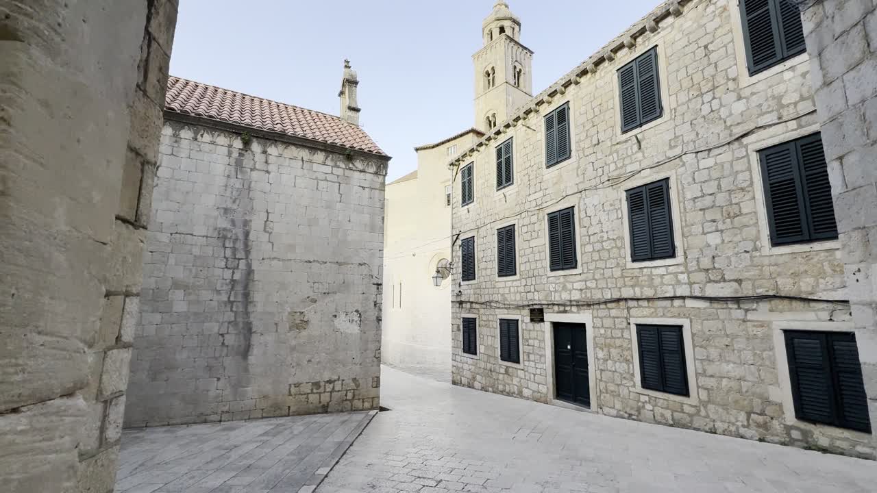 Ripresa cinematografica a piedi attraverso la porta orientale della città vecchia di Dubrovnik con strade vuote e il campanile della chiesa del monastero domenicano che si erge sopra gli edifici storici in pietra calcarea al mattino presto
