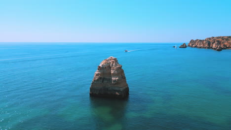 Huge-rock-sticking-out-of-the-ocean-during-the-summer-in-Praia-Dona-Ana-in-the-Algarve-in-Portugal,-aerial-drone-view