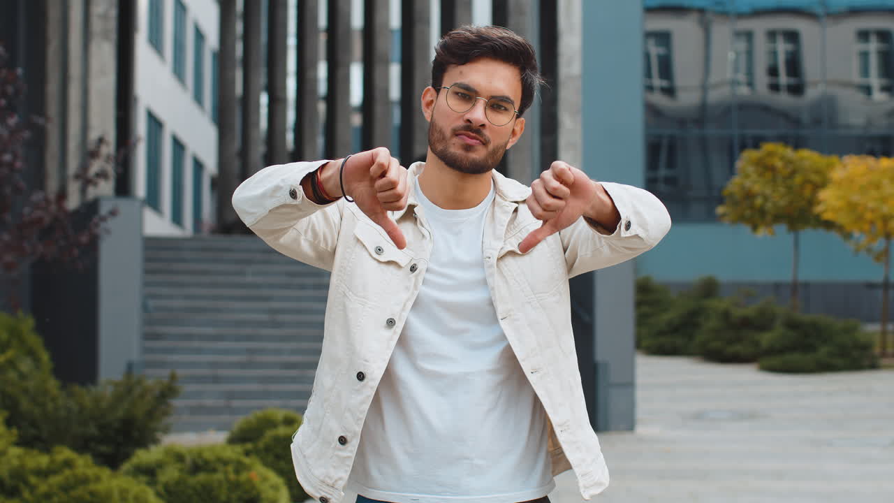 Upset indian man showing thumbs down sign disapproval dissatisfied bad work mistake in urban city