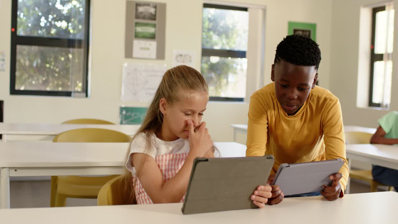 Diverse kids boy coming from right showing tablet, girl shifting and comparing screens in classroom