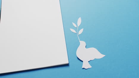 close up of white dove with leaf, white paper and copy space on blue background