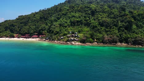 Island-Hill-Huts-in-lush-Jungle-fores,-emerald-waters-lagoon