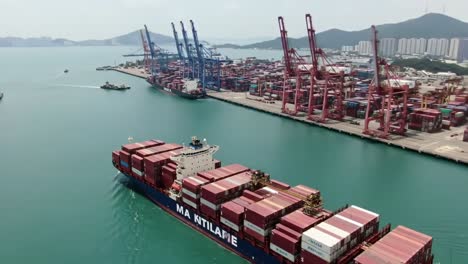 aerial view of a container ship navigating through a busy port, surrounded by cranes and shipping containers in tranquil waters