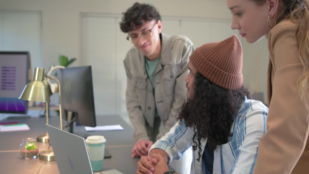 Colleghi diversi che indicano lo schermo di un laptop, si battono il cinque e poi digitano aggiornamenti in ufficio