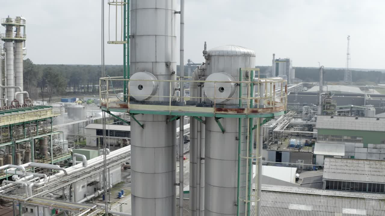 Aerial circling shot focusing on tall, silver industrial distillation columns with platforms and pipes at factory, Veille-Saint-Girons, France
