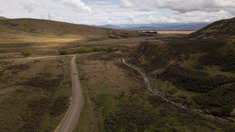 Aerial-footage-of-car-driving-on-Mackenzie-Pass-with-stunning-mountain-views-in-Canterbury,-New-Zealand