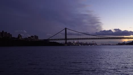 boat crossing the east river with brooklyn suspension bridge and skyline of new york city at distance during epic sunset