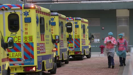 a row of ambulances and health workers stand outside a building placed under covid-19 coronavirus lockdown as they prepare to screen, monitor, and treat large numbers of residents who tested positive