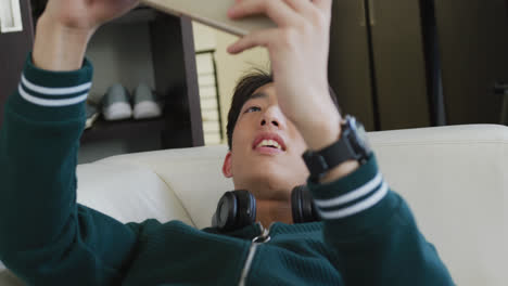 asian boy playing games on digital tablet lying on the couch at home