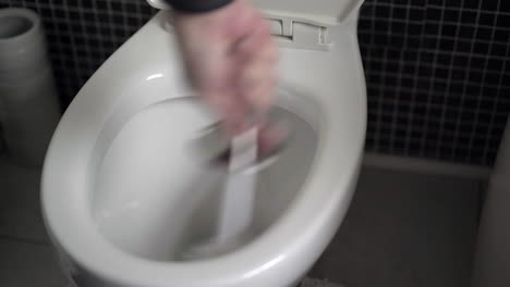 man's hand scrubbing white toilet bowl with a toilet brush