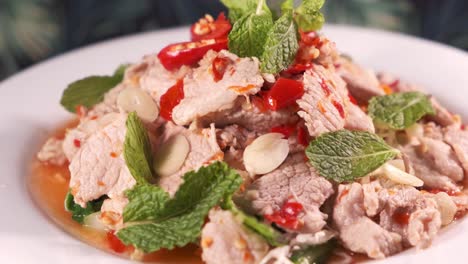 Authentischer-Thailändischer,-Würziger-Schweinefleischsalat-Mit-Roten-Chilis,-Der-Sich-Auf-Einem-Weißen-Teller-Dreht