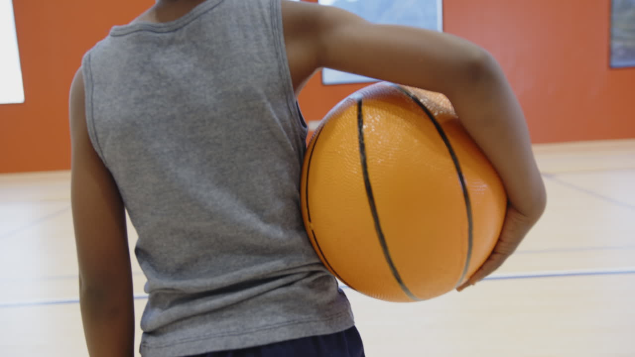 Holding basketball, child in gym wearing gray tank top, ready for game