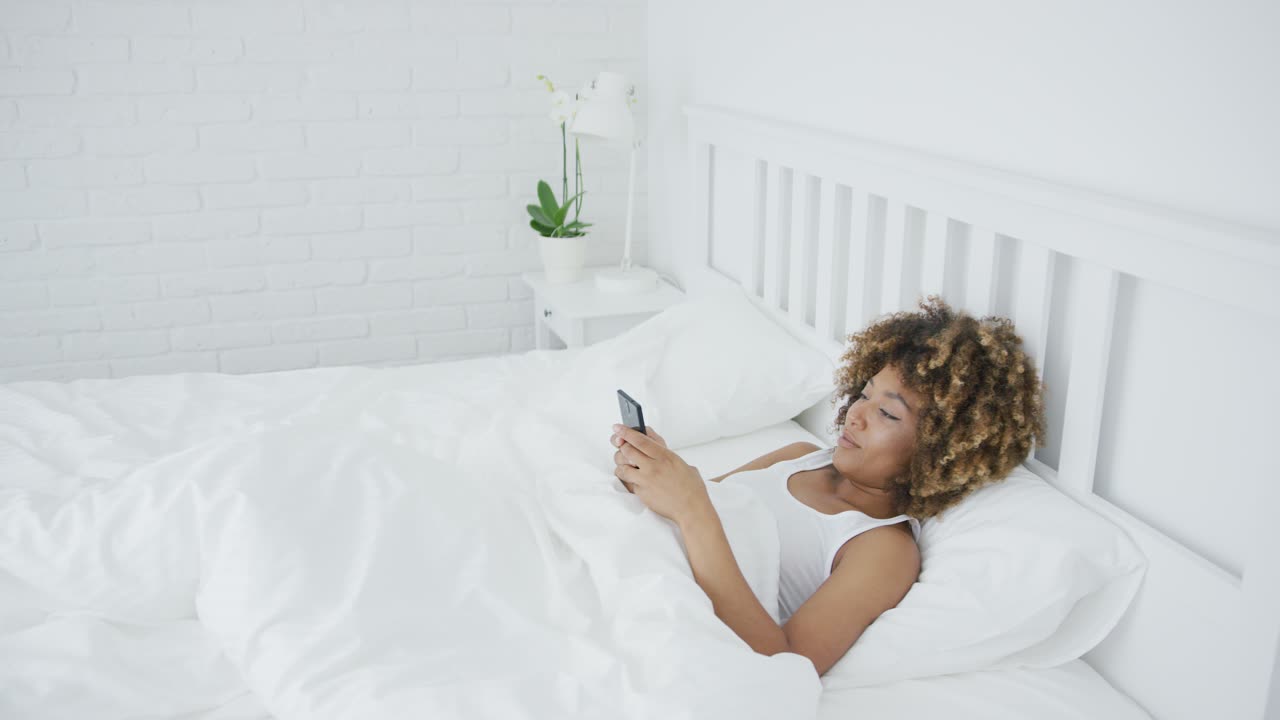 Donna sorridente che si rilassa con il telefono a letto