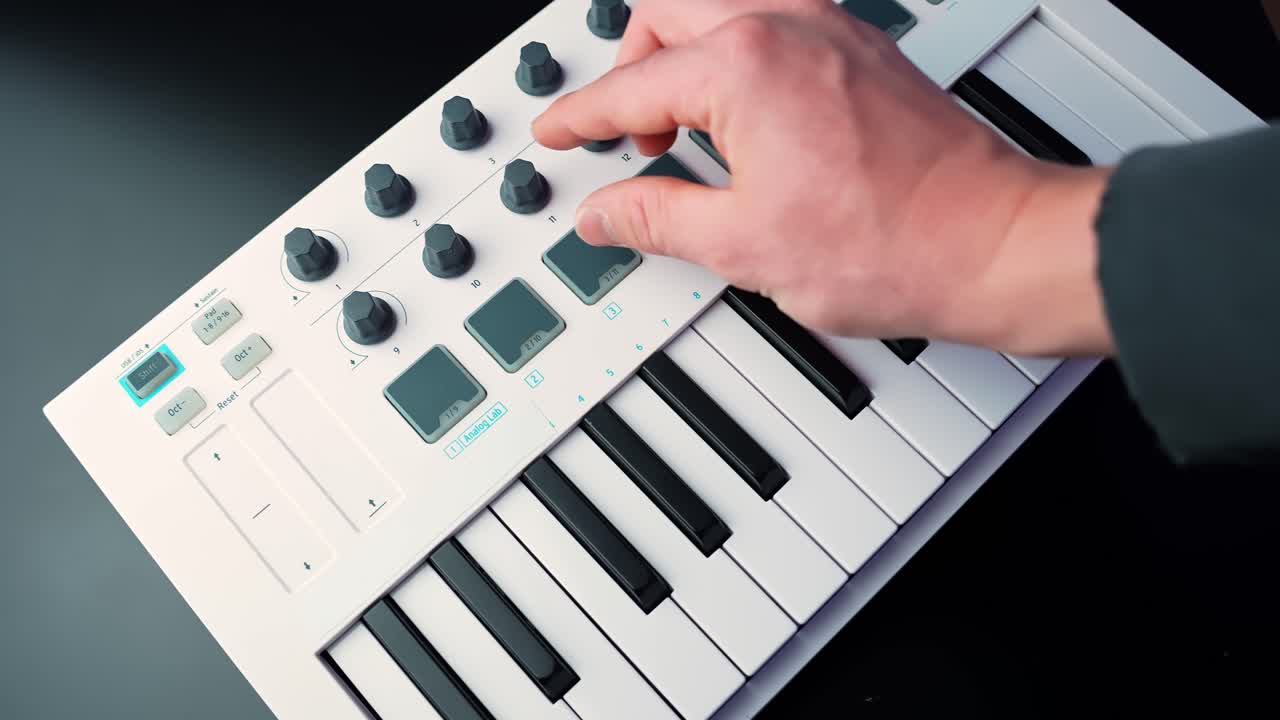 Primo piano di una mano che picchietta i drum pad su un controller tastiera MIDI, attivando campioni per la produzione musicale in uno studio casalingo. Flusso di lavoro elettronico moderno e sound design creativo.