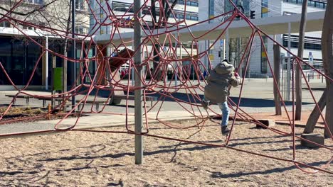 young boy climbing a low rope course in an outdoor park near a shopping mall on a sunny day