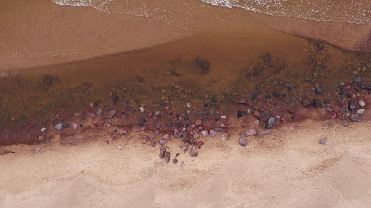 песчаное побережье с каменными валунами и морскими волнами, разбивающимися о песок