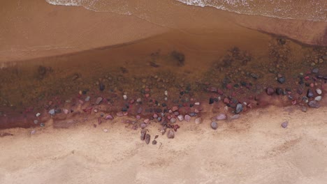 Sandige-Küste-Mit-Steinblöcken-Und-Meereswellen,-Die-Auf-Sand-Krachen