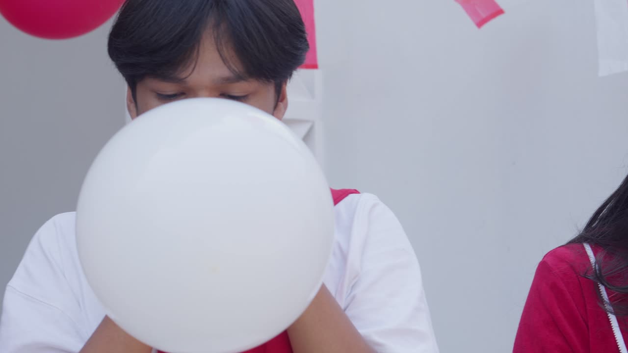 행복한 젊은 아시아 친구들이 인도네시아 독립의 날 대회에서 함께 풍선을 불어넣고 있습니다.