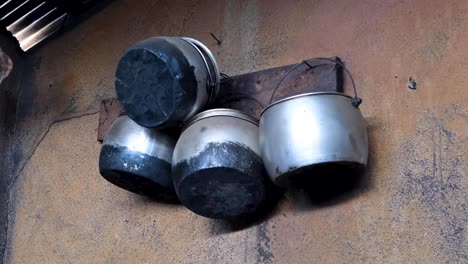 collection of large stainless steel cooking pots hanging on pegs against old rustic wall in rural kitchen