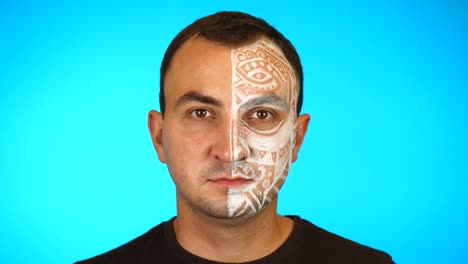 portrait of young man with colored face paint on blue background. professional makeup fashion.