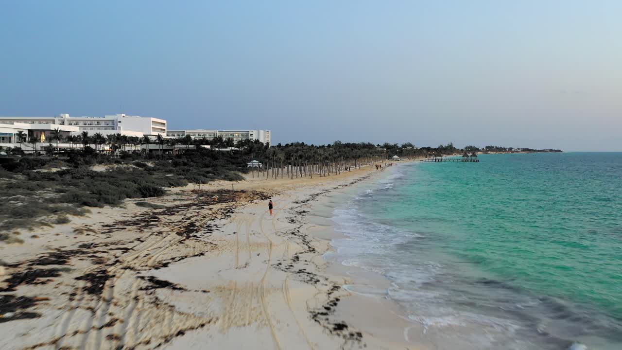 Aerial footage flying along Cancun’s beach at dusk, showcasing a beachfront resort, palm trees, and turquoise waters under the evening sky.